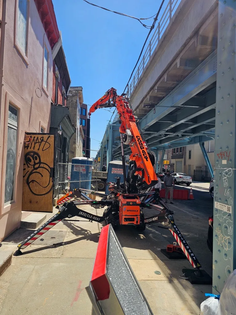 Jekko SPX532.2 mini crane set up on a Philadelphia sidewalk with asymmetric outriggers under an elevated rail line