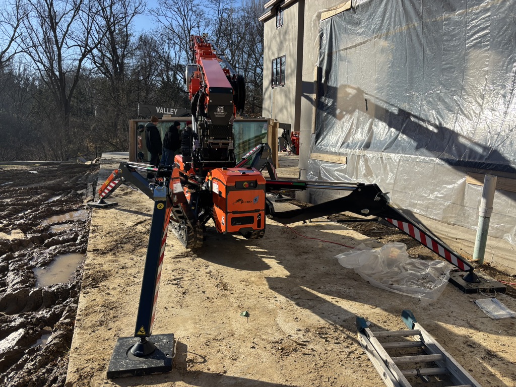 Jekko mini crane setting a curtain-wall glass panel with a vacuum lifter on a residential jobsite
