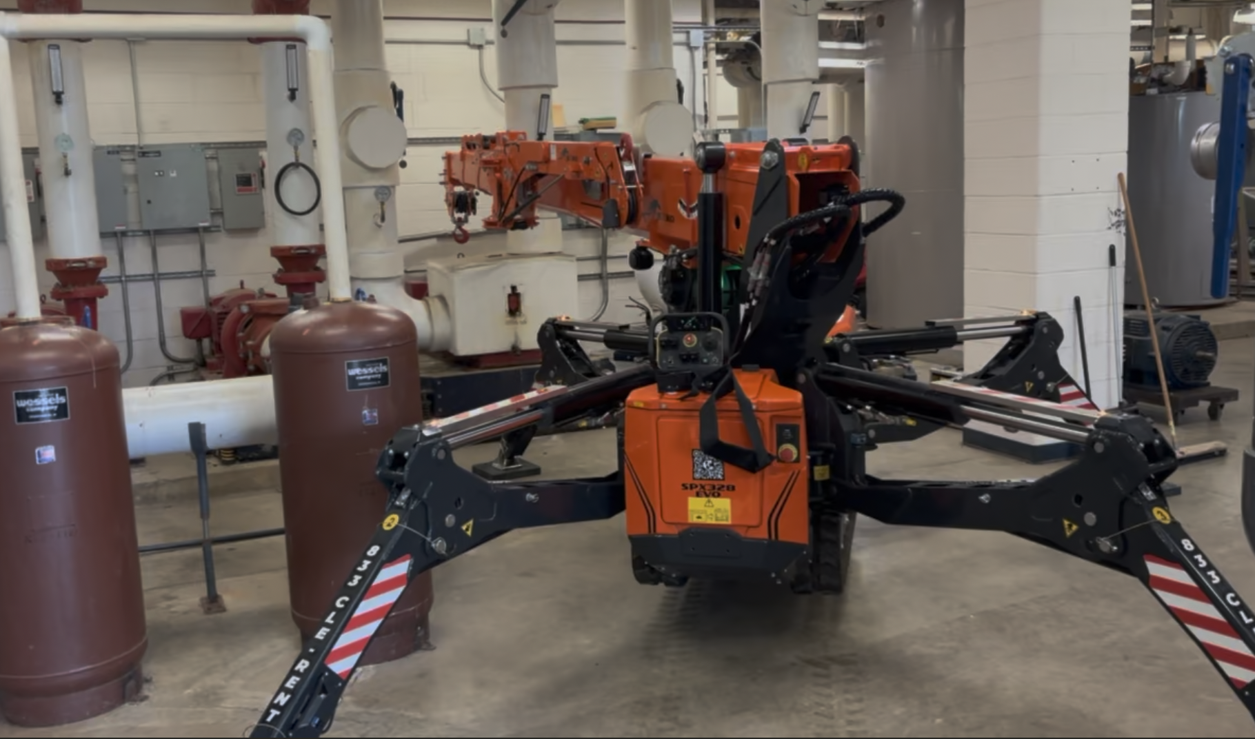 Compact spider crane set up in a mechanical room beside pressure tanks and pumps to rig plant equipment